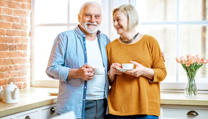 A senior couple holding coffee cups smile for the camera.